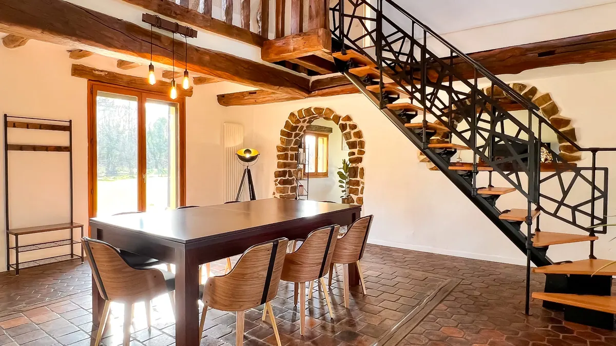 Salle à manger sous les poutres apparentes, escalier et mur de pierre